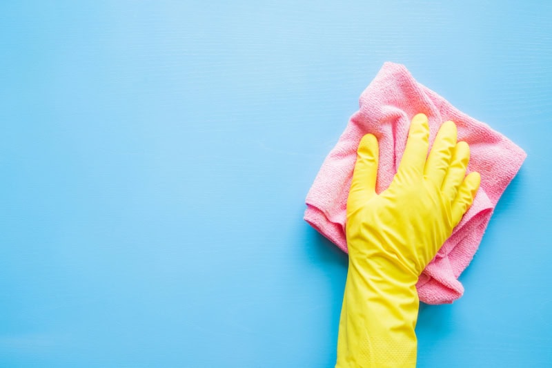 Does an AC Kill Mold? Photo of a hand in a yellow rubber glove, wiping a blue wall or table with a pink cloth.