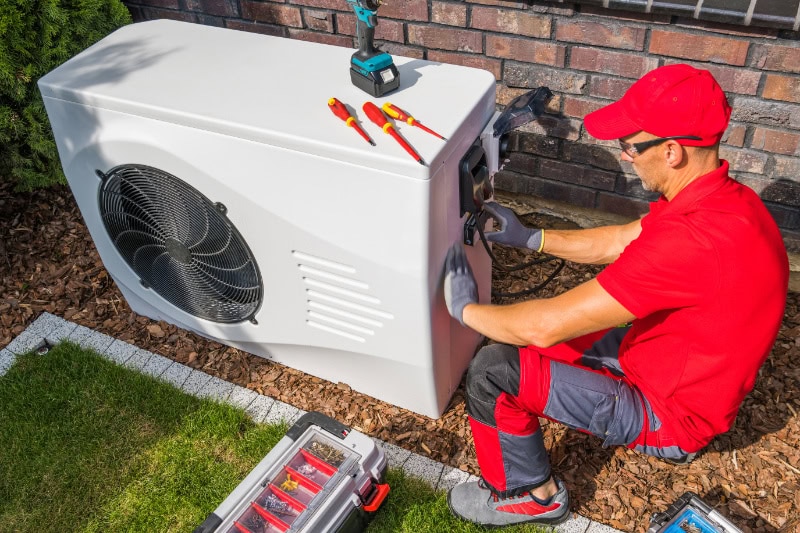 4 Factors to Consider When Buying a Heat Pump. Professional Middle Aged HVAC Technician in Red Uniform.