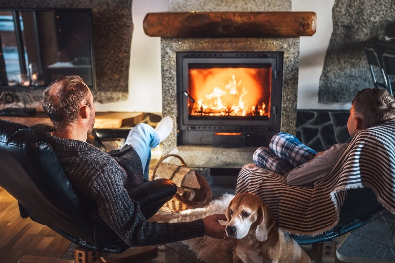 The Basics of Winter Indoor Air Quality. Photo of a father and son sitting in armchairs enjoying the fireplace together.